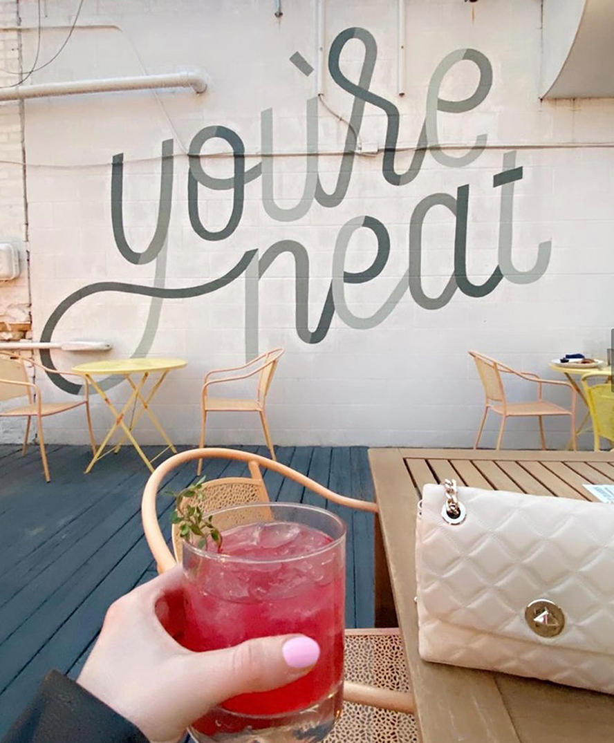 A GR Bucket List team member holds up a cocktail against a wall that says, "You're neat."