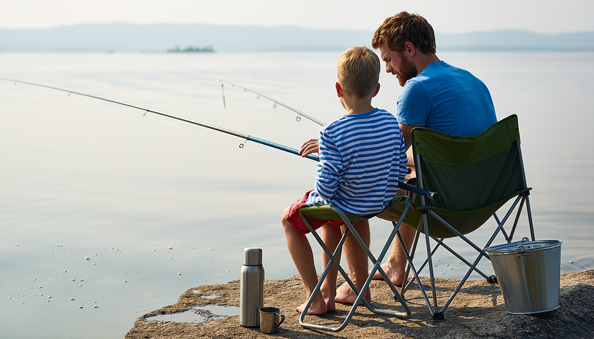 A father and son sit and fish together.