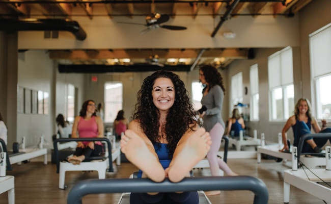 Dark Haired Woman smiling with her feet on a pilates machine