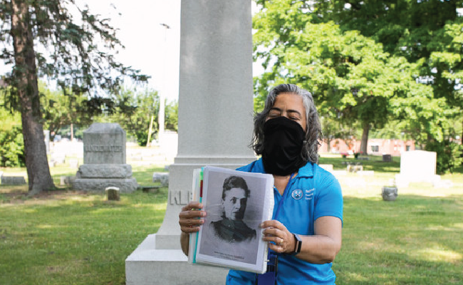 Tour guide with black mask on with an old photo on display at a cemetery